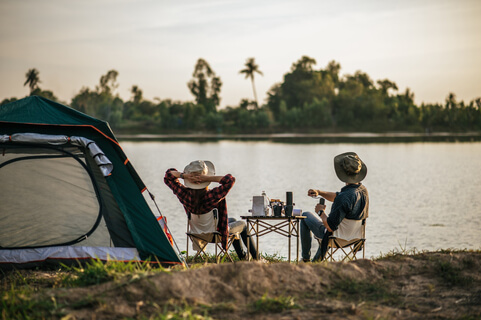 Leben auf einem Campingplatz - Paar am Ufer eines Flusses oder Sees sitzend